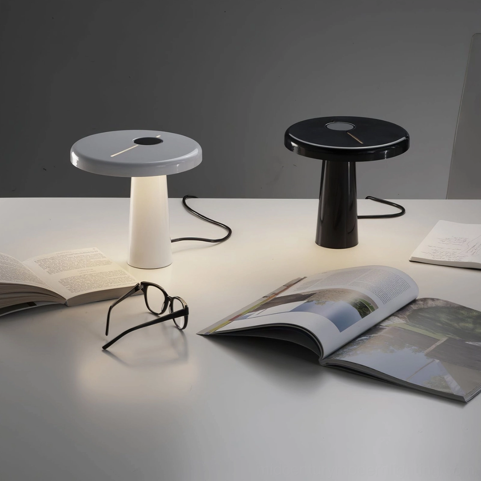 Two asymmetrical Hoop LED table lamps in black and white sitting on home office desk with magazines and glasses