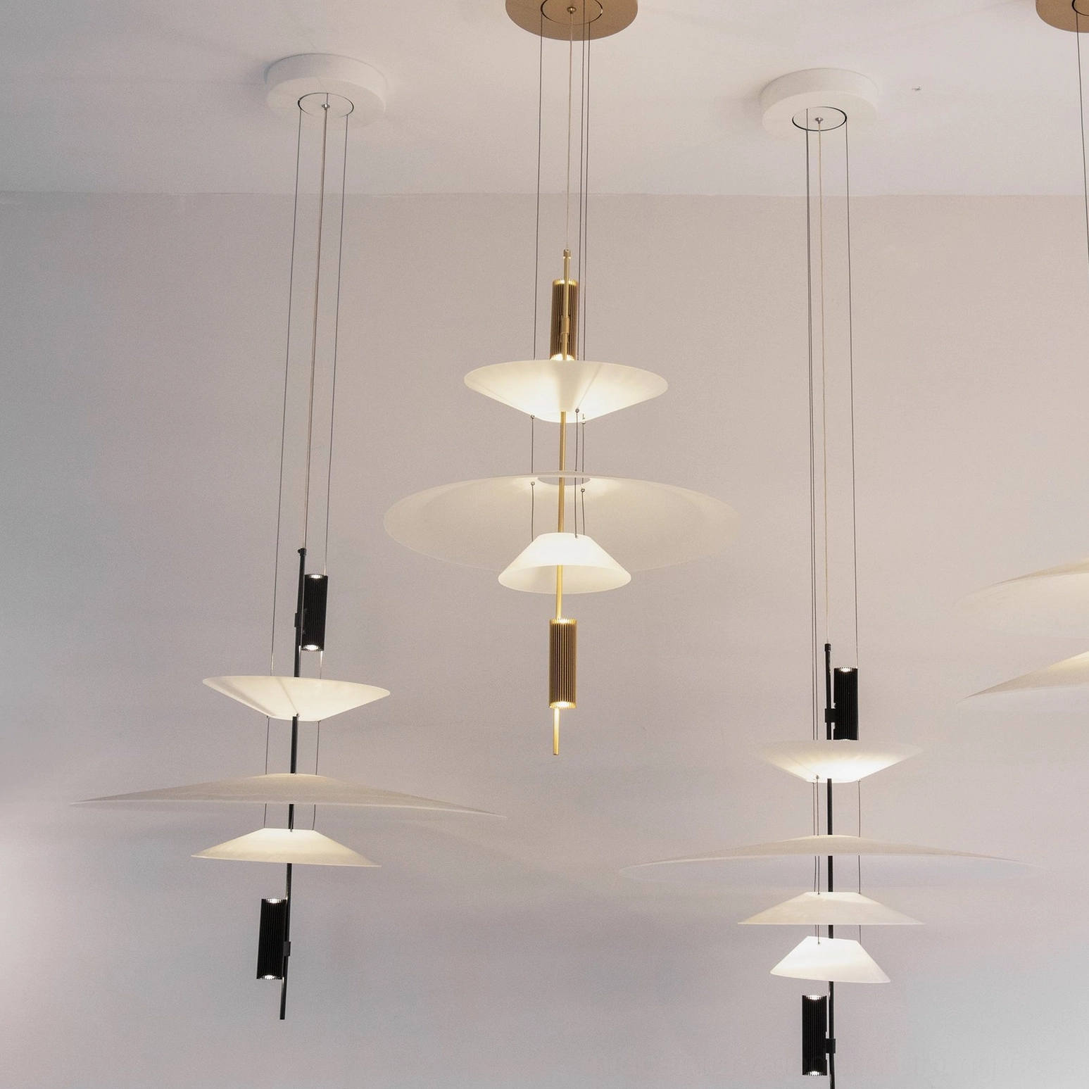 Multiple Hover Disc chandeliers with mixed gold and black metal hardware and matching white translucent discs