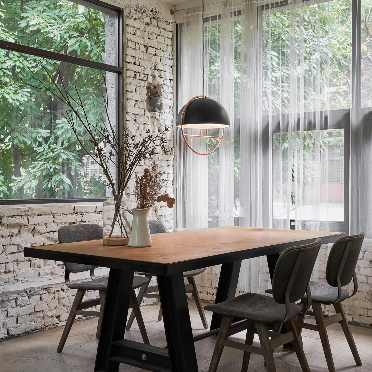 Black matte dome pendant light with rose gold frame mounted over wooden dining table in rustic brick dining room
