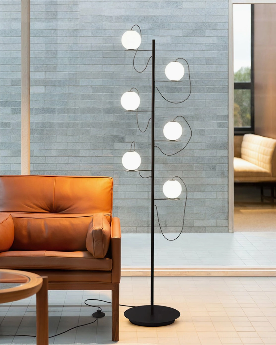 Mid-century modern floor lamp with illuminated frosted glass globes in living space with tan leather armchair and industrial minimalist aesthetic