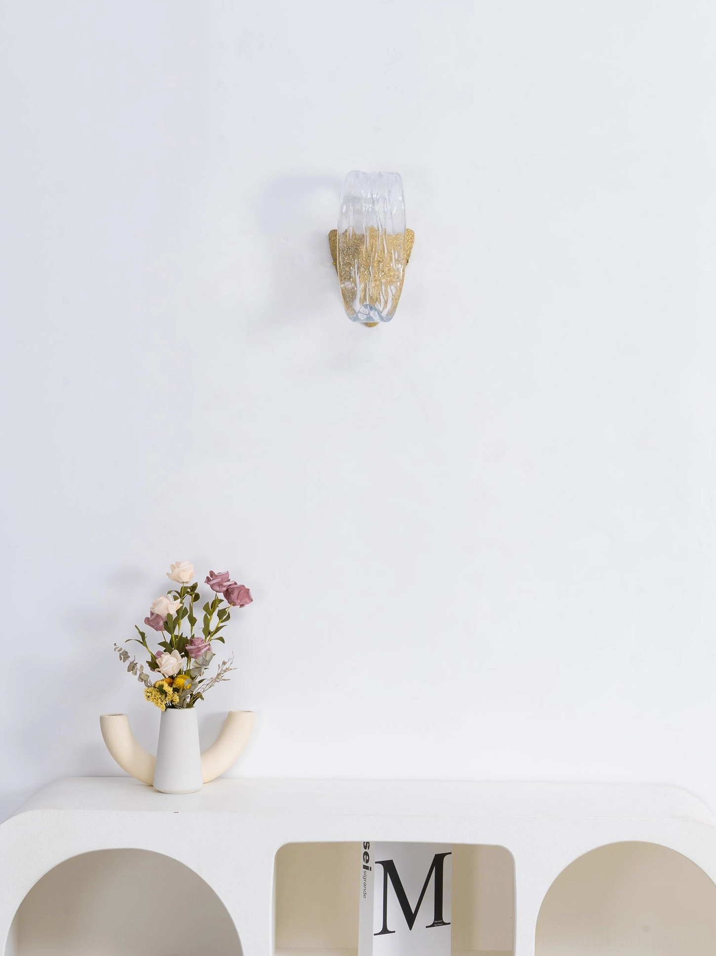 Icarus wall sconce in situ showing architectural brass framing with crystal glass element