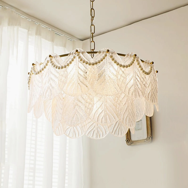 Illuminated tiered frosted glass leaf chandelier glowing with warm light near window in French romantic interior, elegant vintage pendant lighting