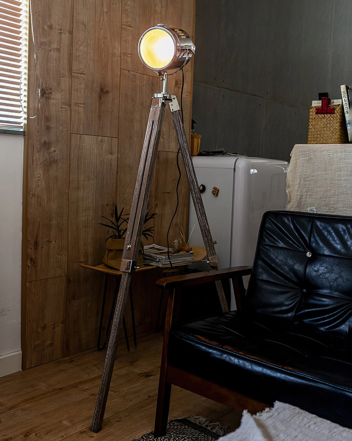 Adjustable spotlight floor lamp illuminated in retro living room with leather sofa and wooden panel wall, three-quarter front angle