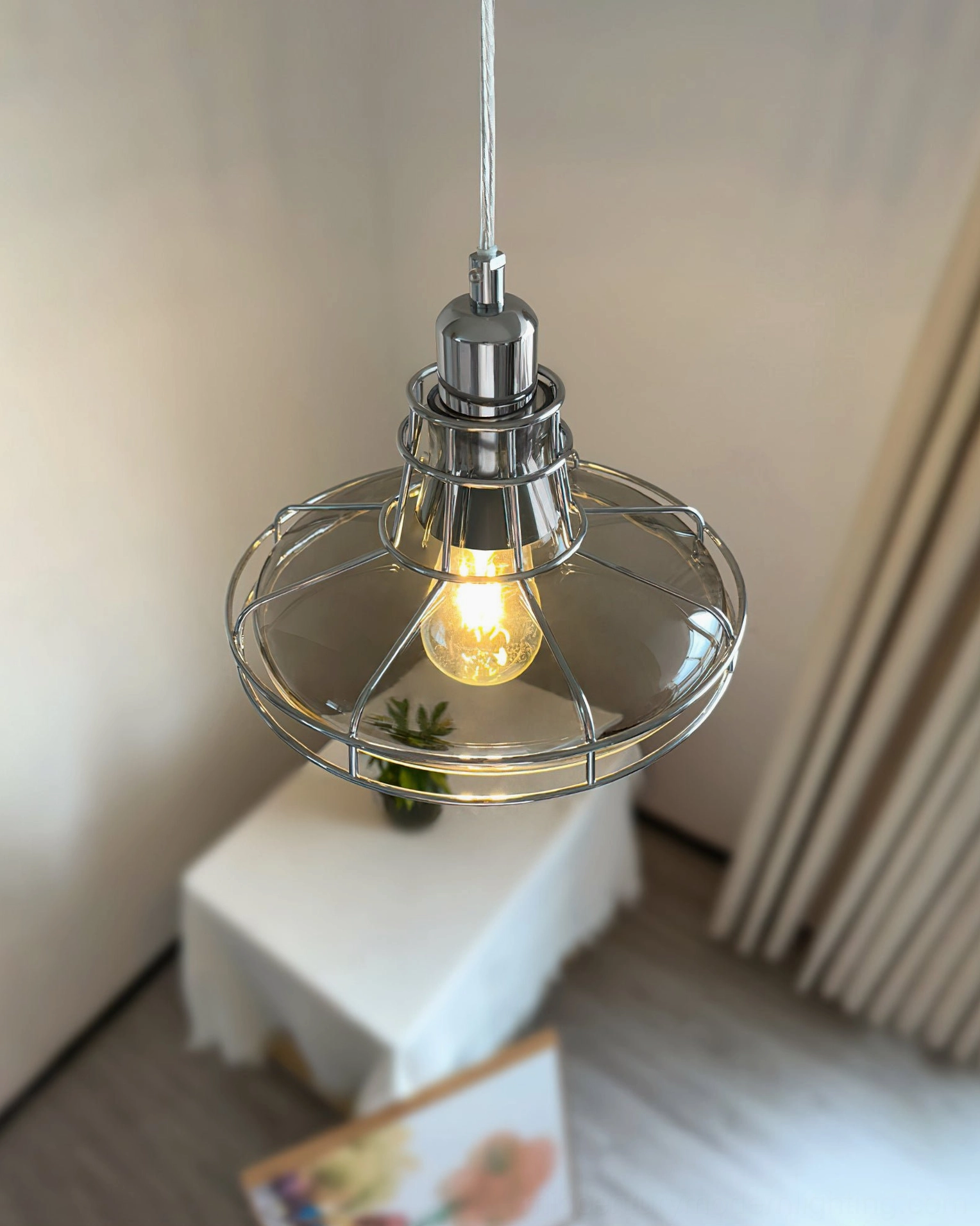 Industrial chrome pendant glowing with warm yellow bulb in cozy corner space, vintage aesthetic side view