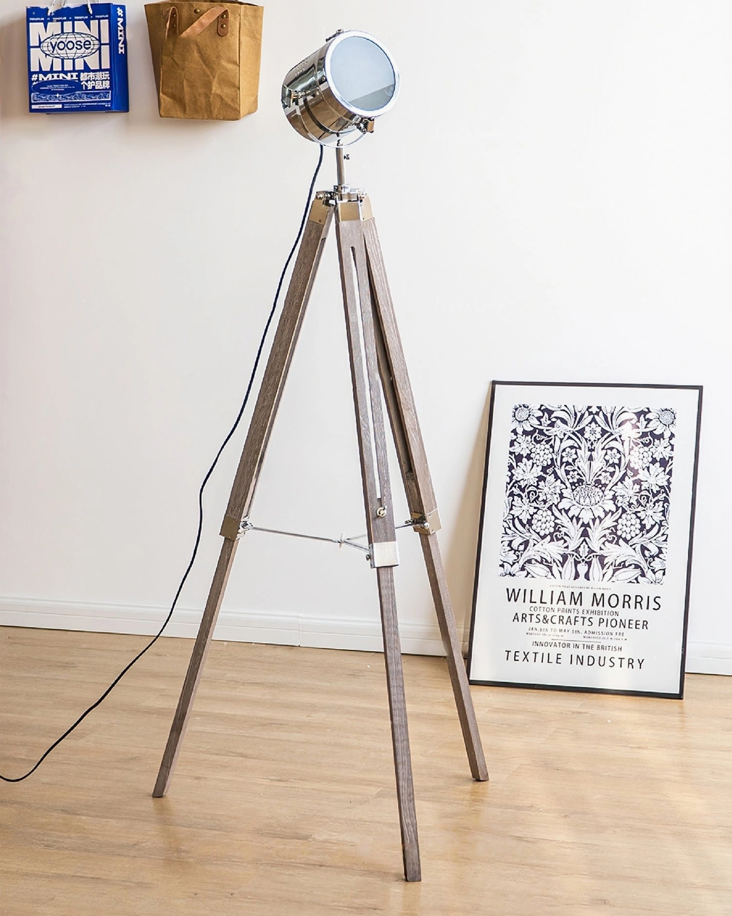 Slim industrial tripod floor lamp with adjustable spotlight in minimalist home office with wall art, polished chrome and natural wood construction