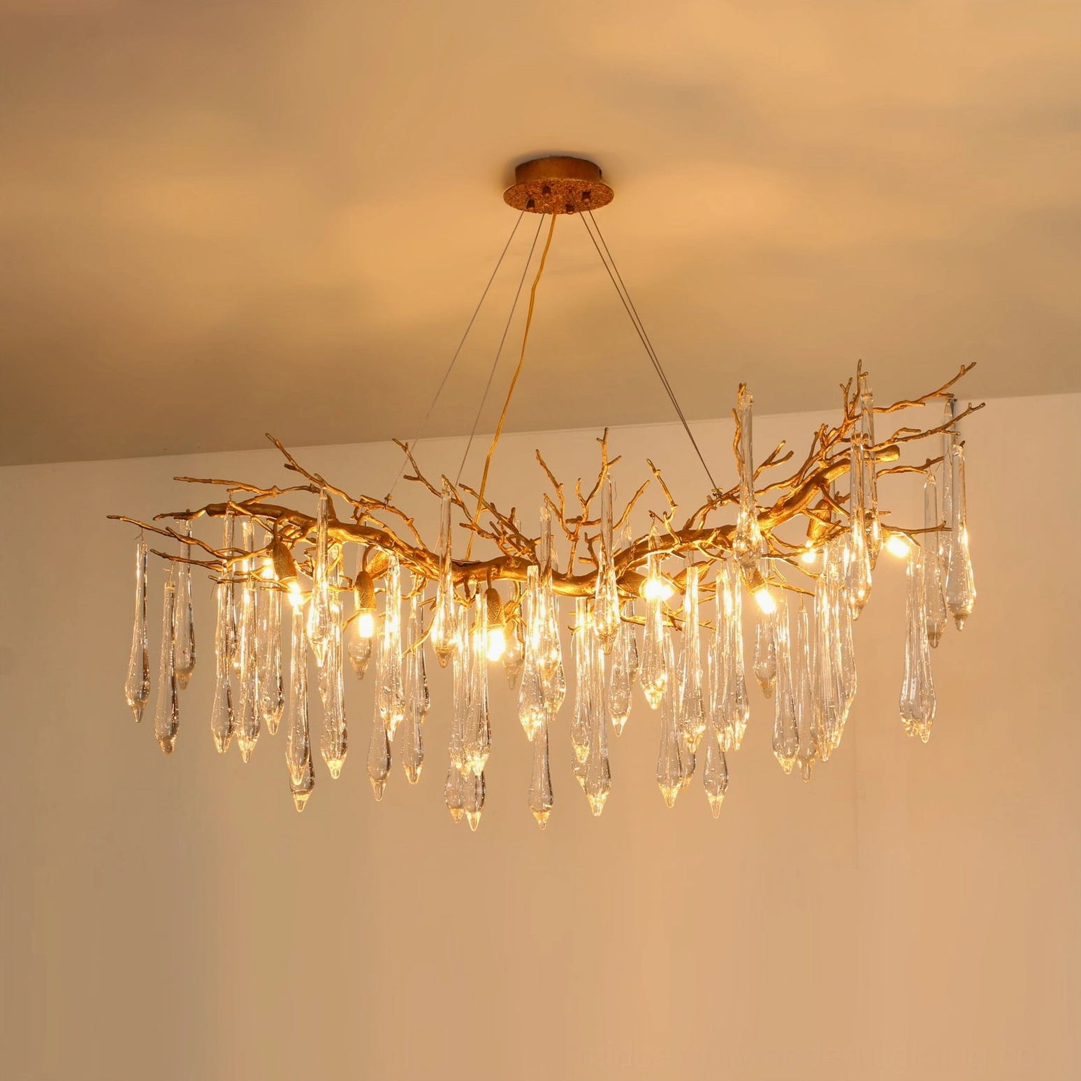 Janae illuminated brass chandelier installed on warm-toned residential ceiling, glowing ambient light through crystal elements