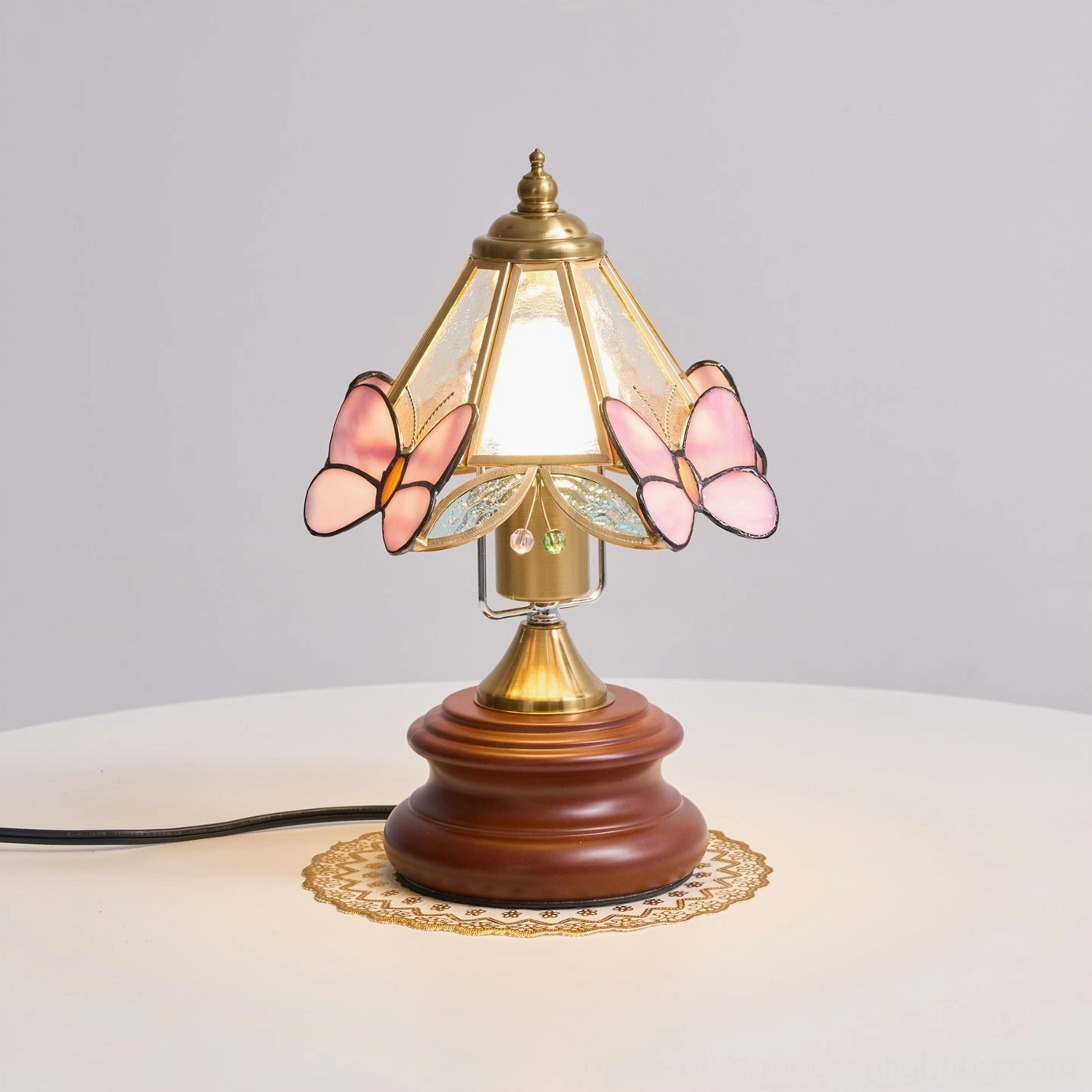 Jenny Butterfly Stained Glass Table Lamp illuminated front view on white side table showing pink butterfly details and warm light