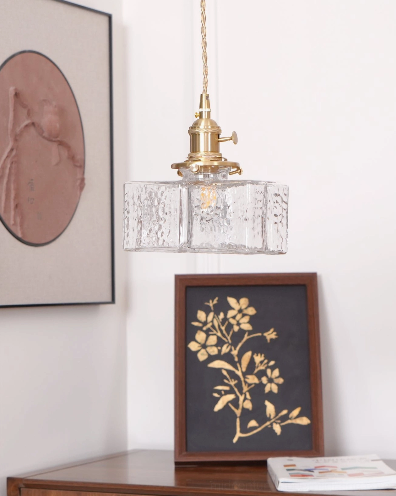 Single jewel brass pendant light with clear hammered glass shade and brass frame illuminated against neutral studio background