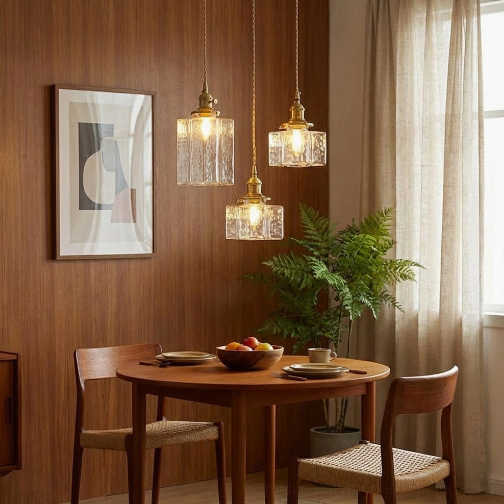 Cluster of three jewel brass pendant lights photographed at side angle in minimalist vintage dining space with wood table