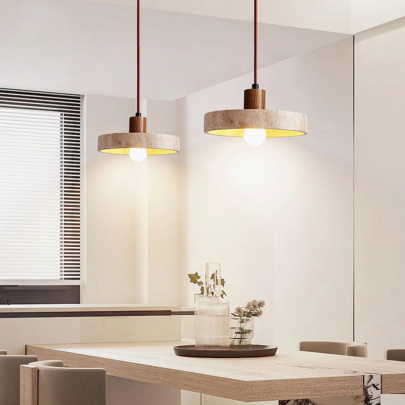 Two matching Kairi travertine pendants installed in modern minimalist dining room with overhead lighting