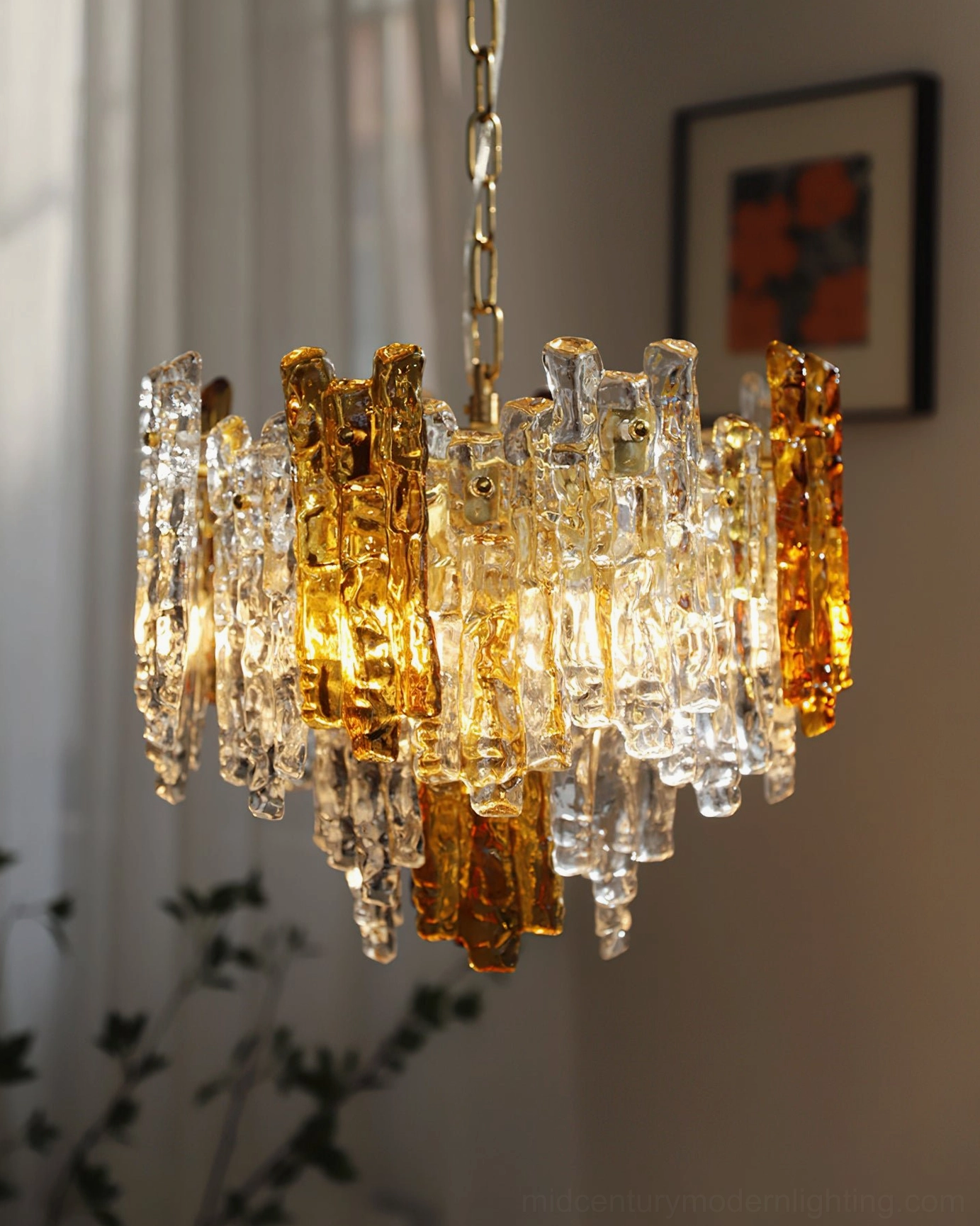 Kalmar lit dual-tone pendant chandelier glowing with warm golden light showing textured glass detail and brass hardware