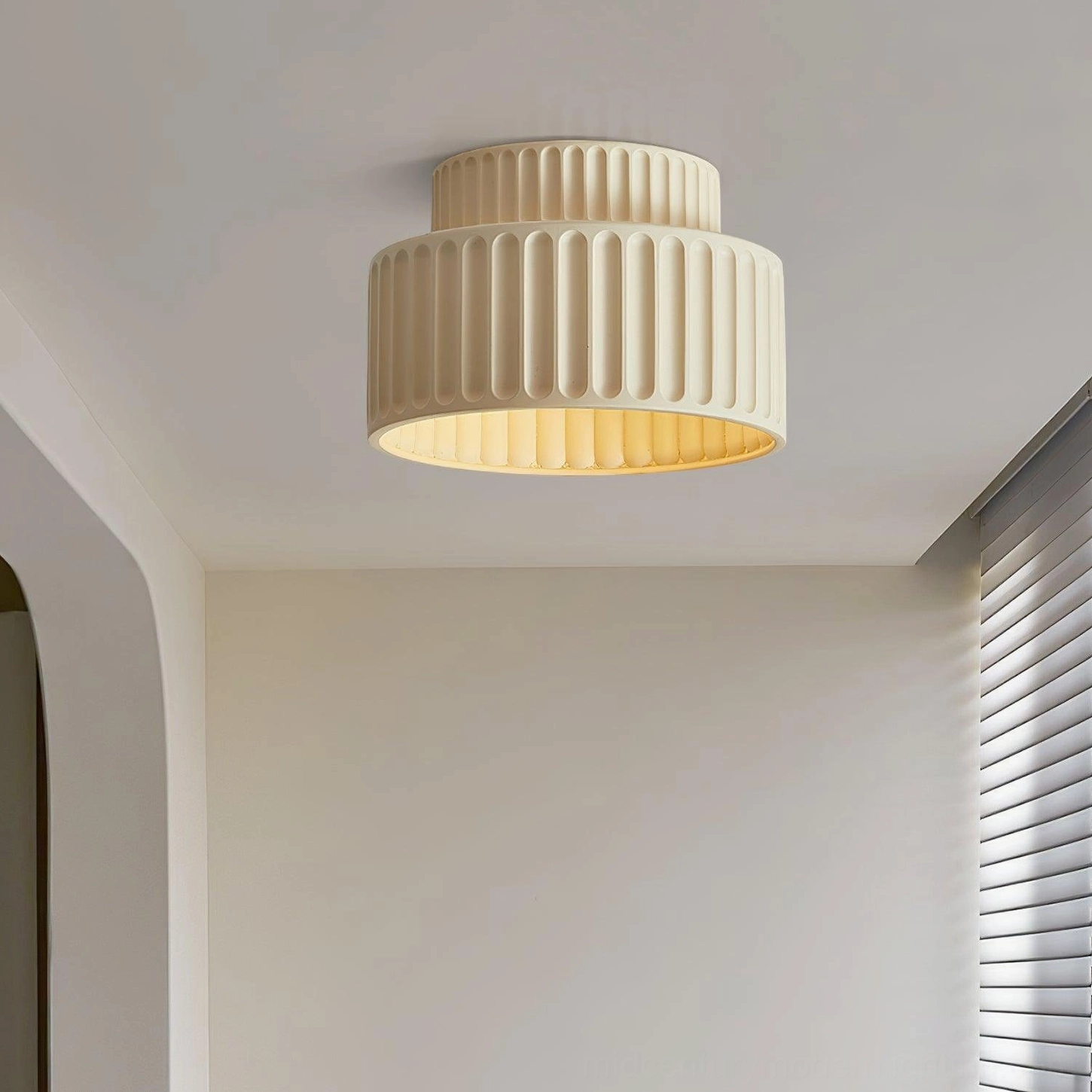 Cream Kami ribbed ceiling lamp low-angle view in minimalist modern hallway, showing warm interior ambient glow