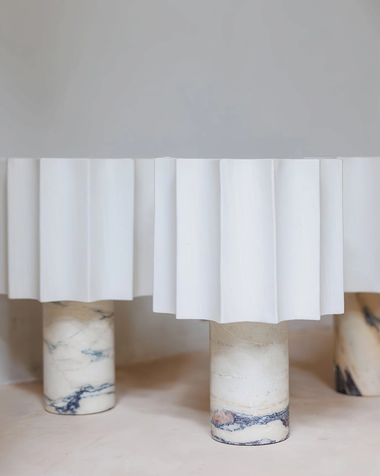 Collection of Kane cordless table lamps displayed on shelf, white pleated shades with various uniquely-veined Calacatta marble bases