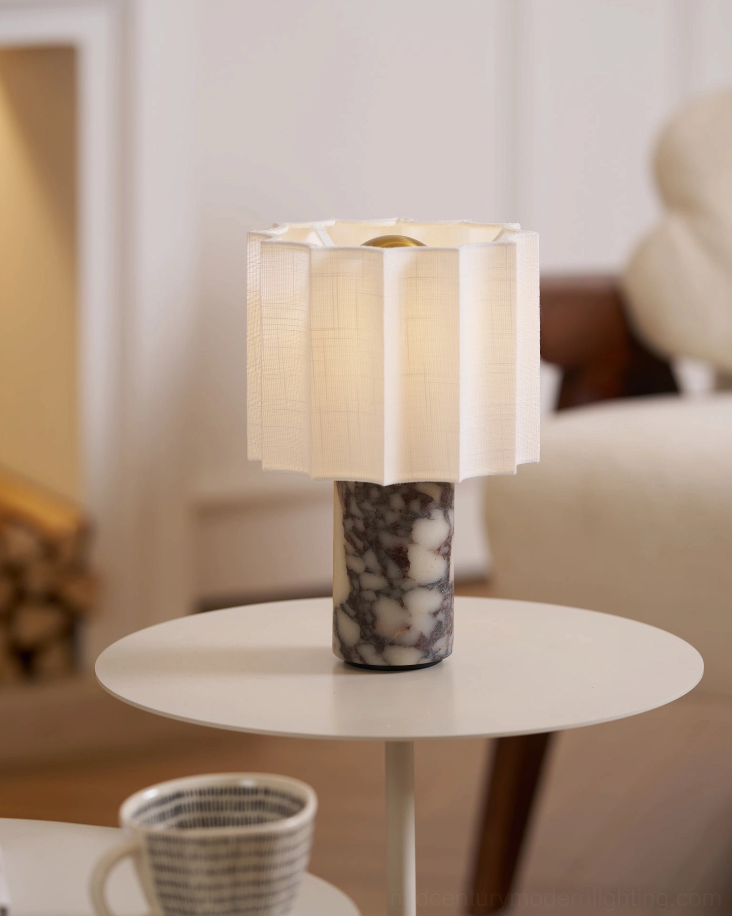 Kane battery-powered table lamp glowing on living room side table, three-quarter view showing white pleated shade and patterned marble cylinder