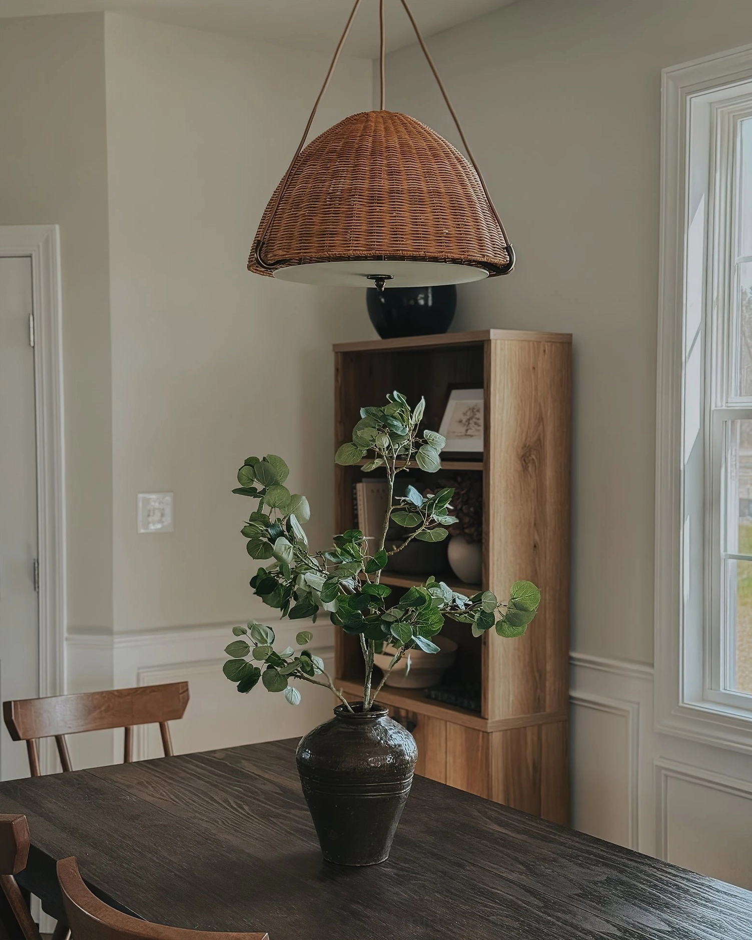 Kash woven rattan pendant light illuminating minimalist warm neutral dining area with wooden furniture