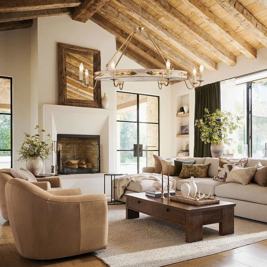 Kayleigh chandelier suspended from wooden vaulted beams in rustic farmhouse living room with stone fireplace and leather seating
