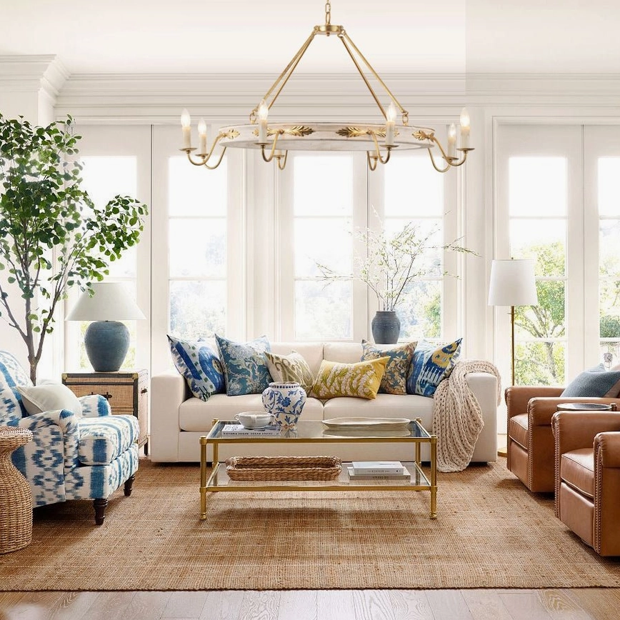 Kayleigh chandelier hanging in bright sunlit living room with bay windows, mixed pattern throw pillows, glass coffee table, and decorative plants