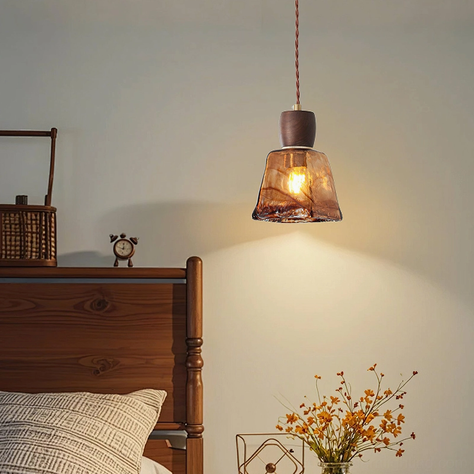 Keju tapered amber glass pendant with walnut wood fixture and twisted brown cord beside wooden headboard