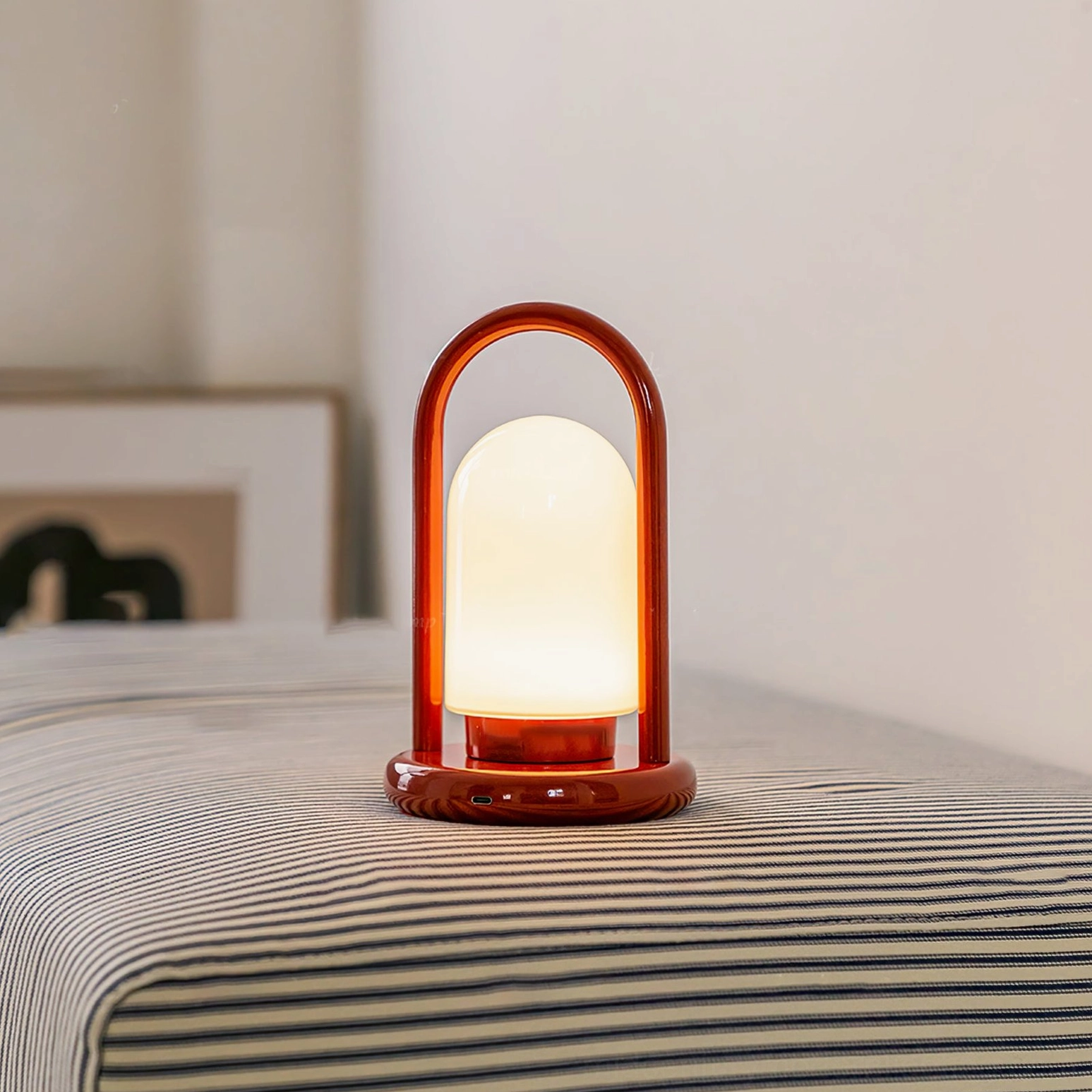 Kero portable lamp lit on bedroom nightstand, casting warm glow over striped bedding
