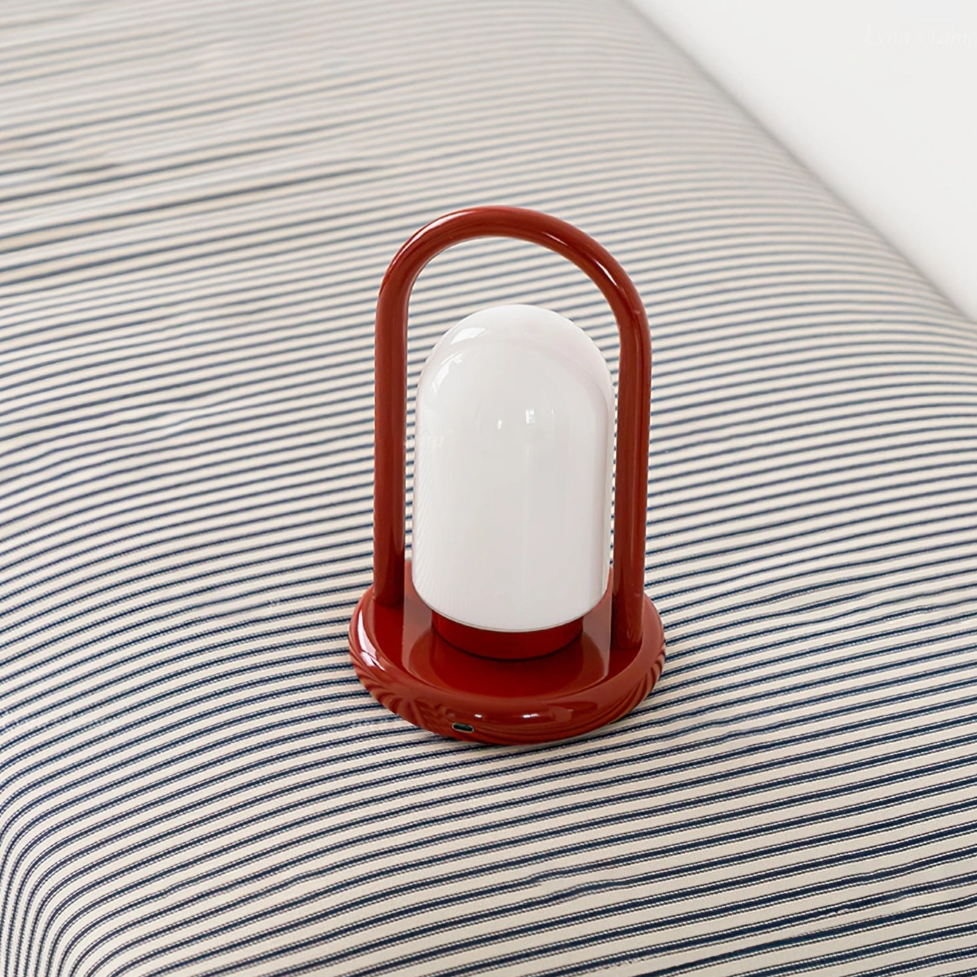 Kero portable table lamp with red metal frame and base on striped bedding, minimalist retro design