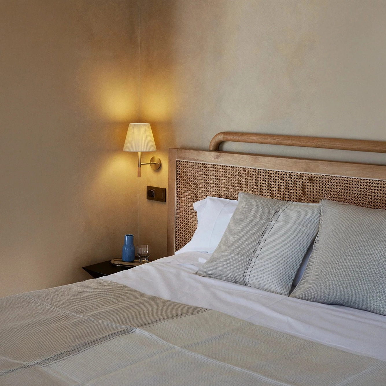 Kilkee bedside wall lamp in rustic bedroom setting with rattan headboard and neutral color palette