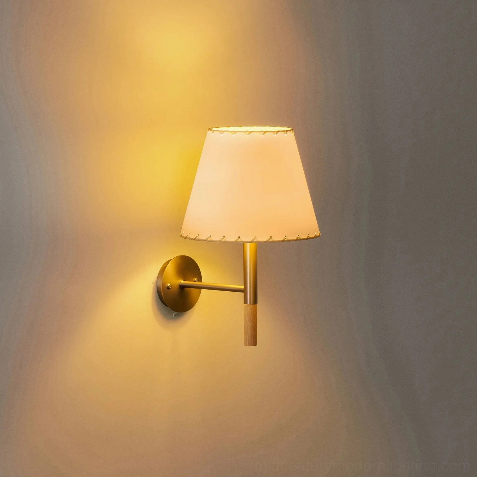 Kilkee wall sconce mounted on interior wall with warm brass nickel finish and glowing ambient light