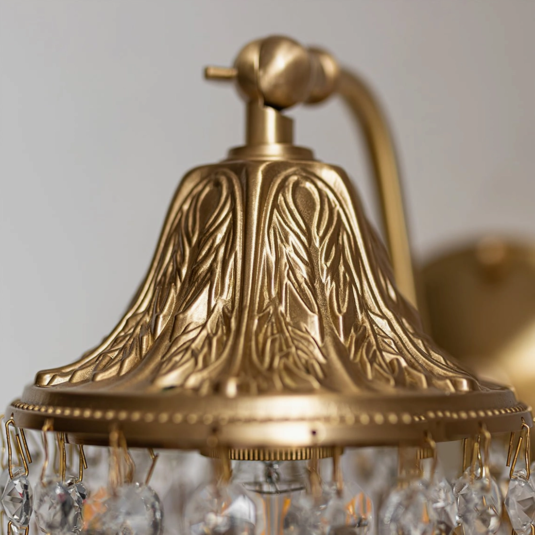 Close-up macro detail of Kristall wall lamp showing leaf-embossed brass base and precisely arranged crystal pendants