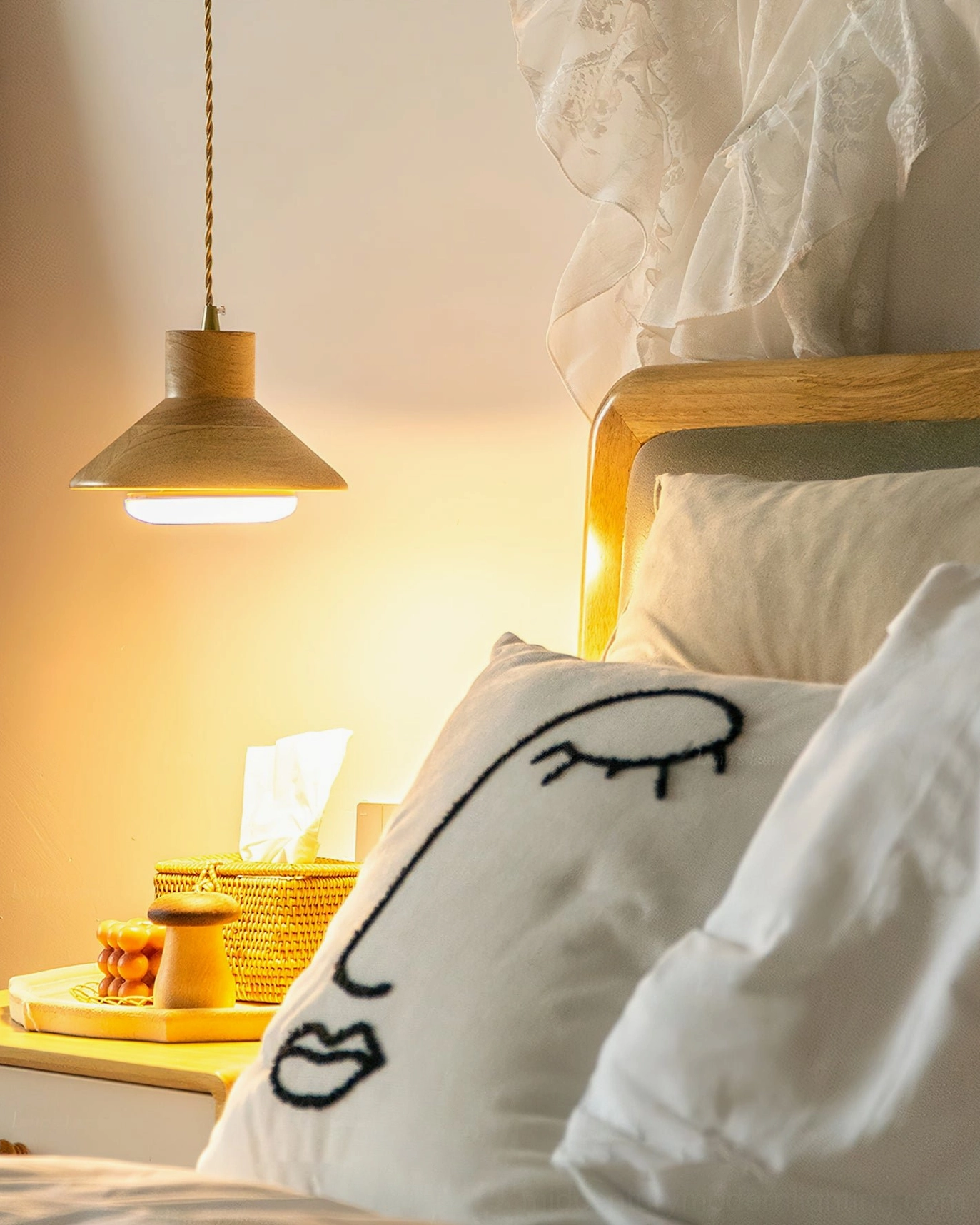 Lander pendant light glowing warm yellow from low angle with face-embroidered pillows and bedroom decor