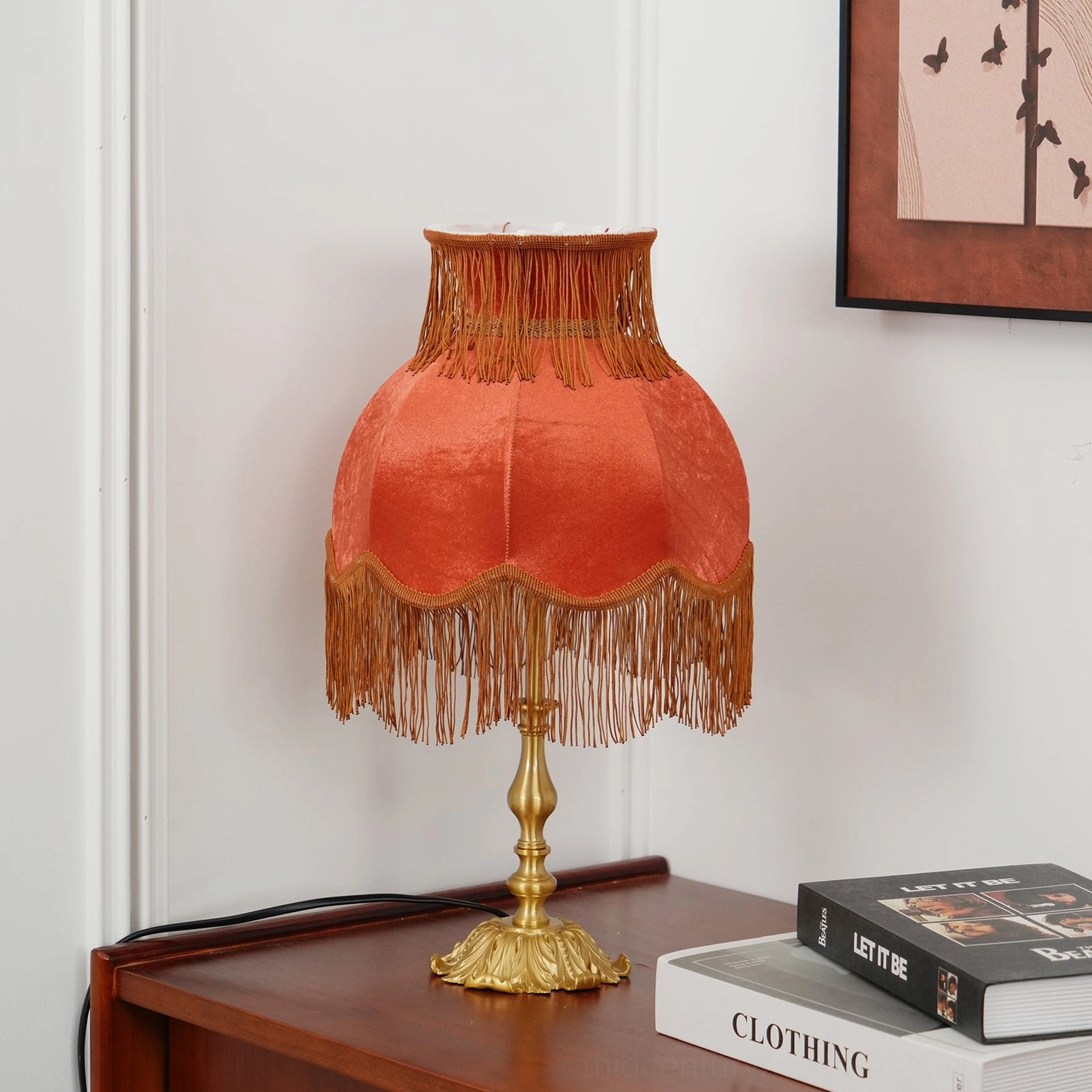 Lanna red fabric tassel table lamp on bedroom wooden side cabinet warm orange glow brass base books wall art