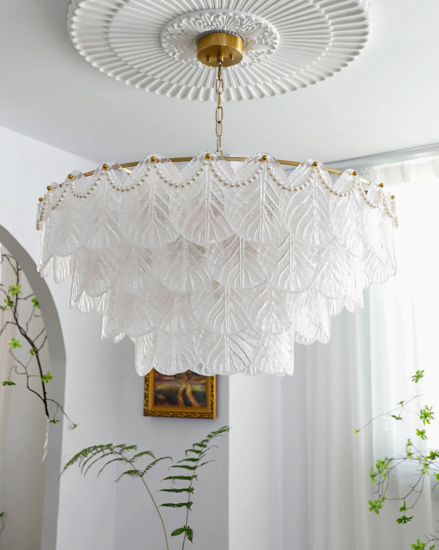 Wide-angle view of large-scale tiered glass leaf pendant lamp in bright interior space with arched architectural details, French country modern styling