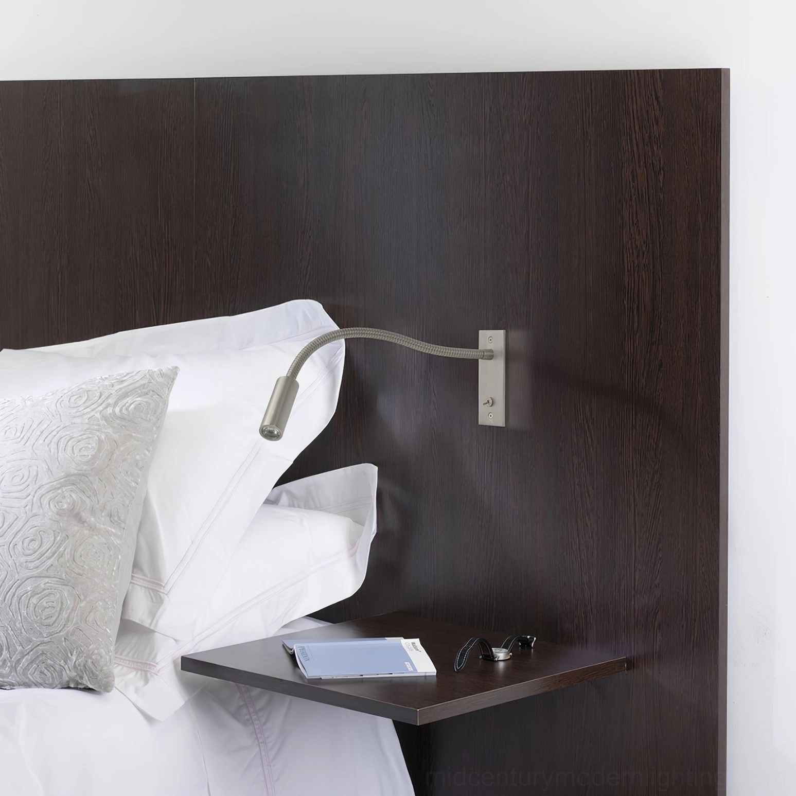 Matte black gooseneck wall lamp mounted bedside in hotel-style bedroom, compact wall design