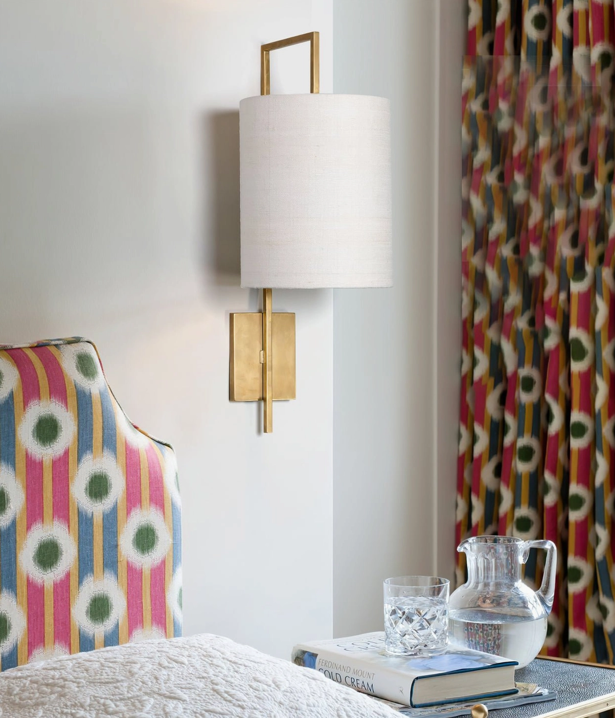 Lewes brass wall sconce with white shade in cozy bedroom ambient lighting