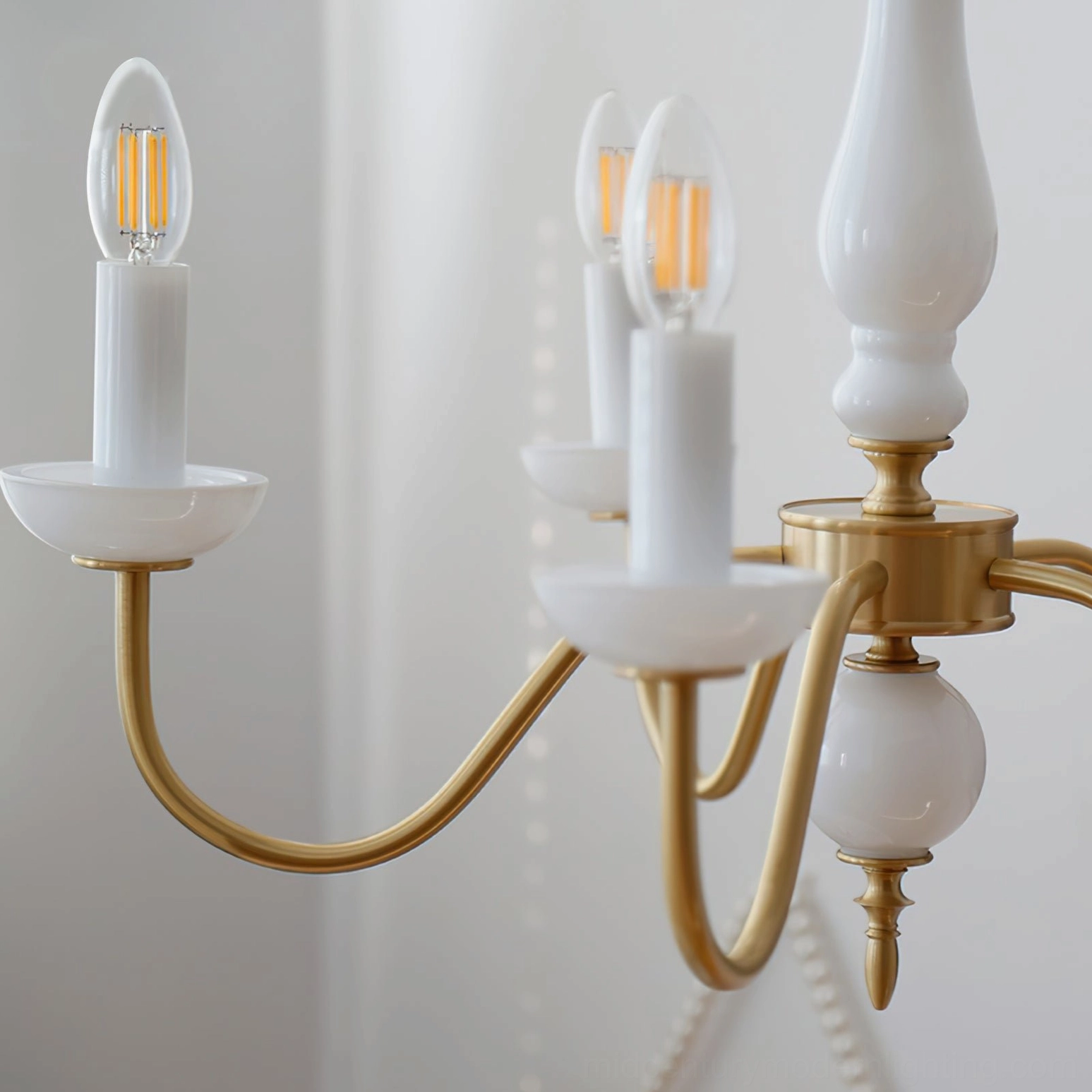 Close-up detail of curved brass chandelier arms with white ceramic candle cup holders