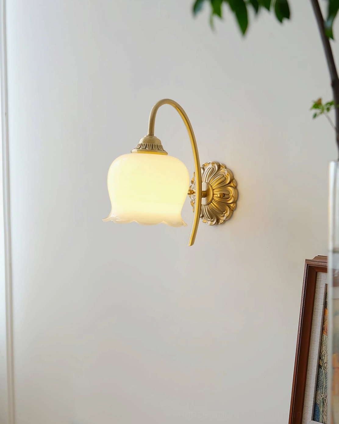 Unlit wall lamp with ornate brass mounting plate and frosted glass shade beside framed wall art