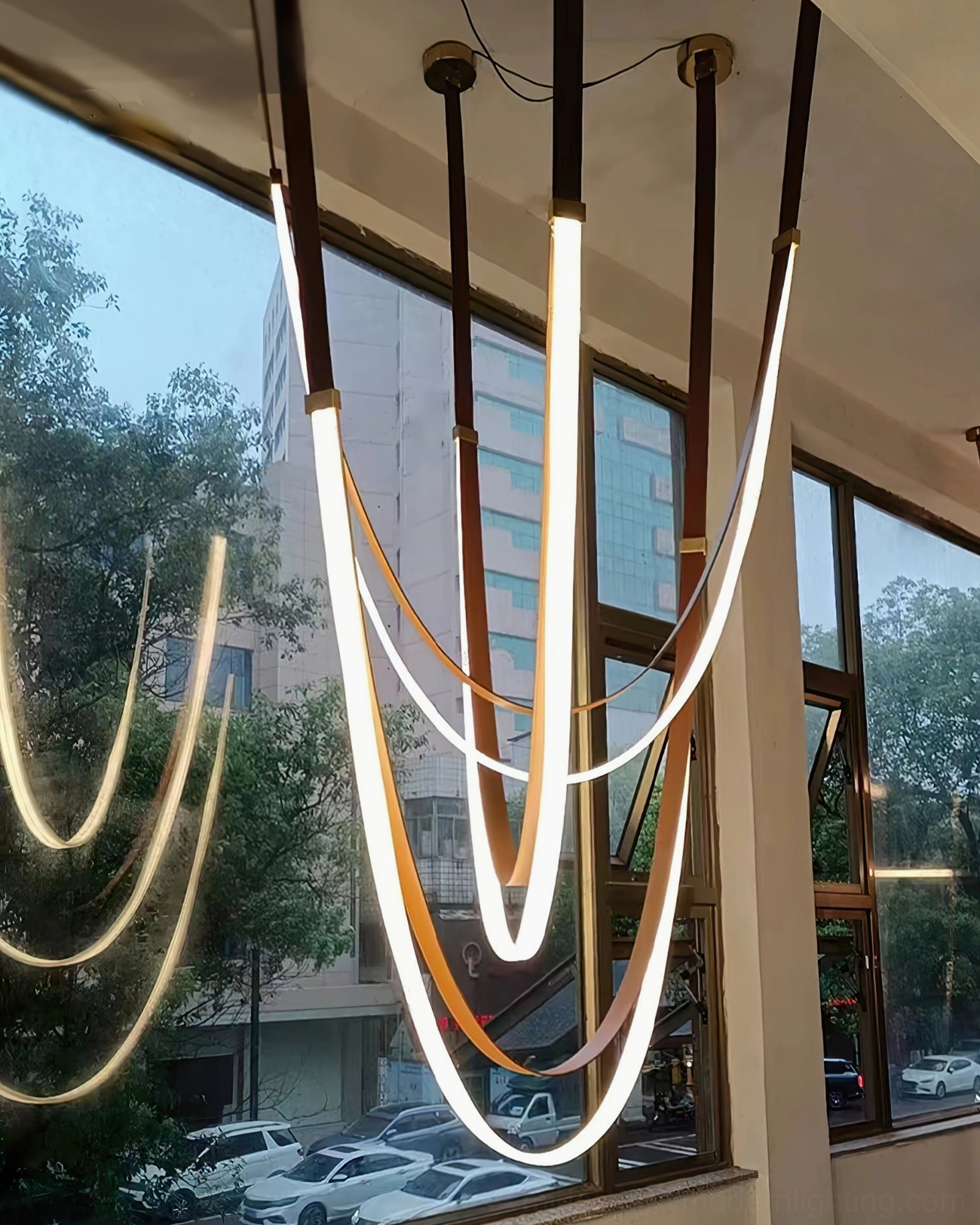 Hanging LED linear pendant light with warm glowing LED tubes and exposed ceiling hardware in modern interior space