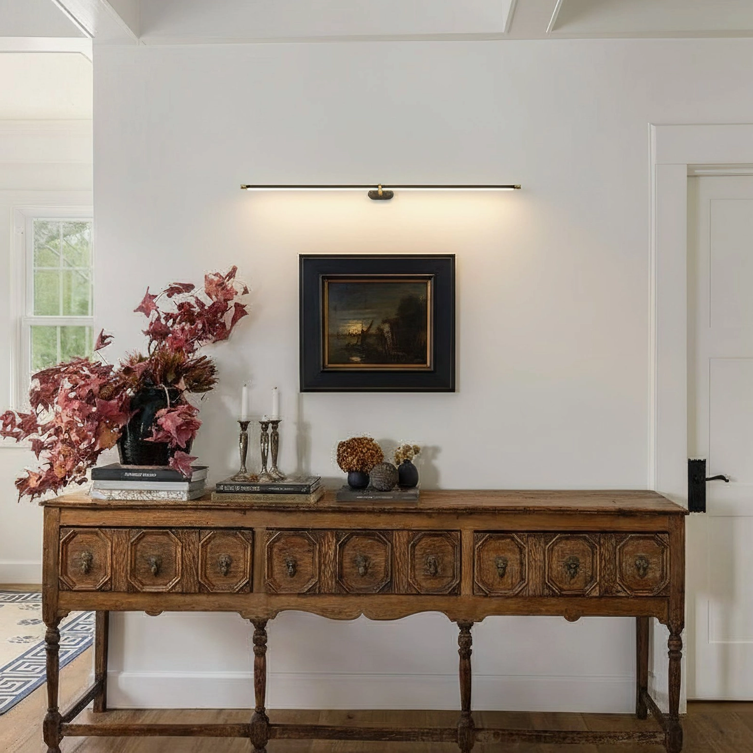 Minimalist linear wall lamp installed in vintage entryway above wooden console table with framed artwork
