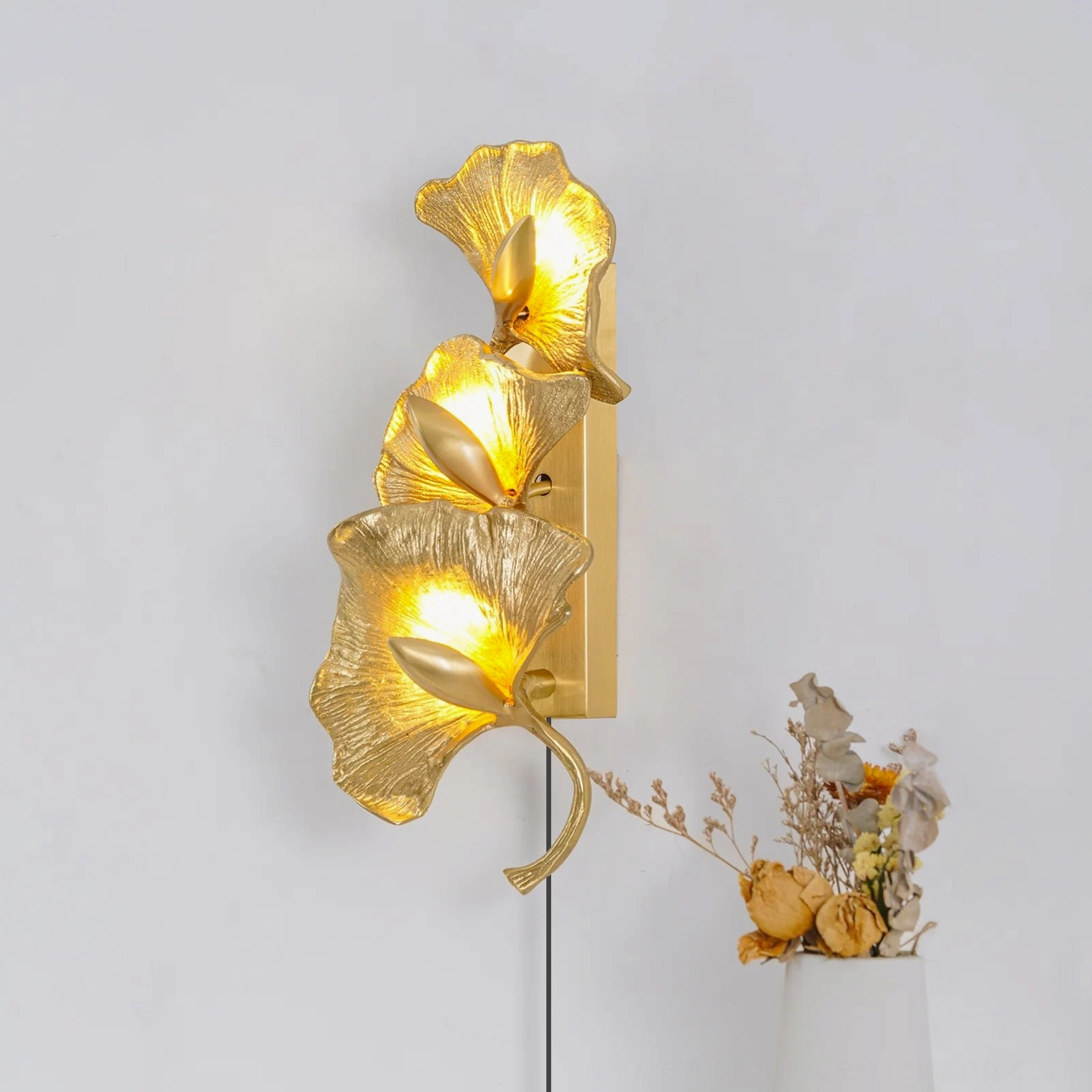 Illuminated ginkgo leaf wall lamp casting warm ambient light in home setting with dried flowers