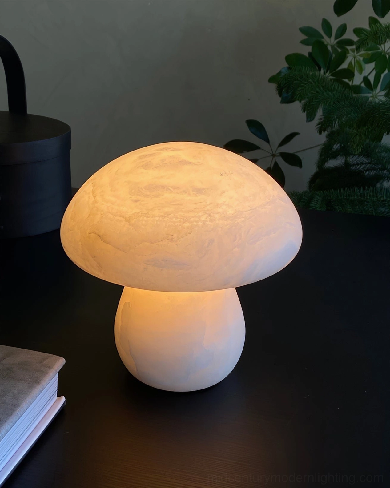 Illuminated mushroom alabaster lamp glowing with warm amber light on dark table surrounded by green foliage plants