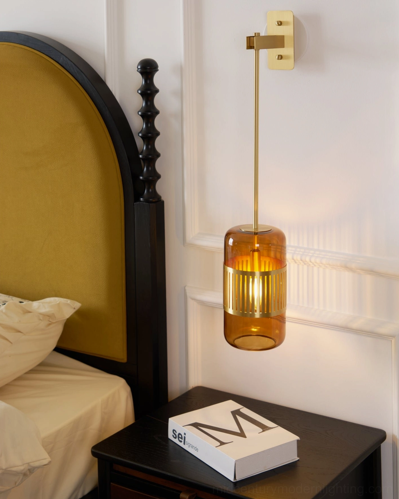 Lizak amber glass wall sconce mounted beside vintage bedroom headboard, three-quarter angle showing brass framework and glass clarity