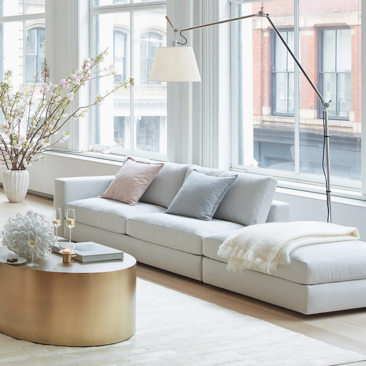 Long reach swing arm floor lamp in bright modern living room with floor-to-ceiling windows and L-shaped sofa