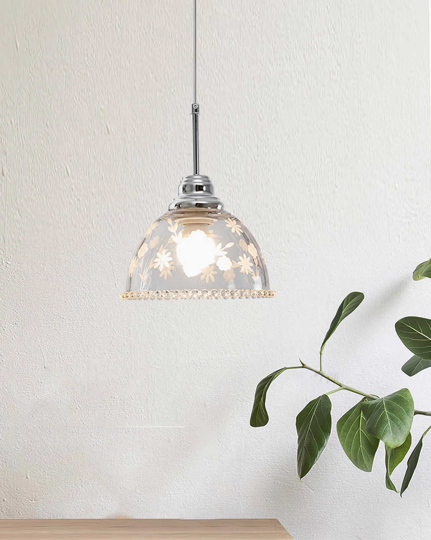Lucinda floral etched pendant lamp beside green plant, side view showing chrome rod suspension