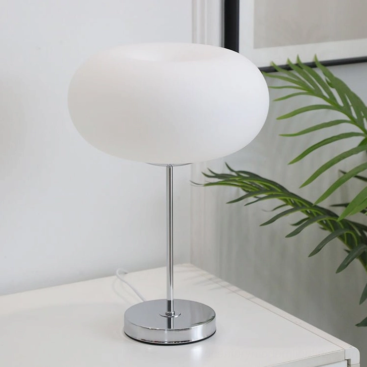 Modern minimalist table lamp with oval frosted milk white shade, side perspective on white dresser