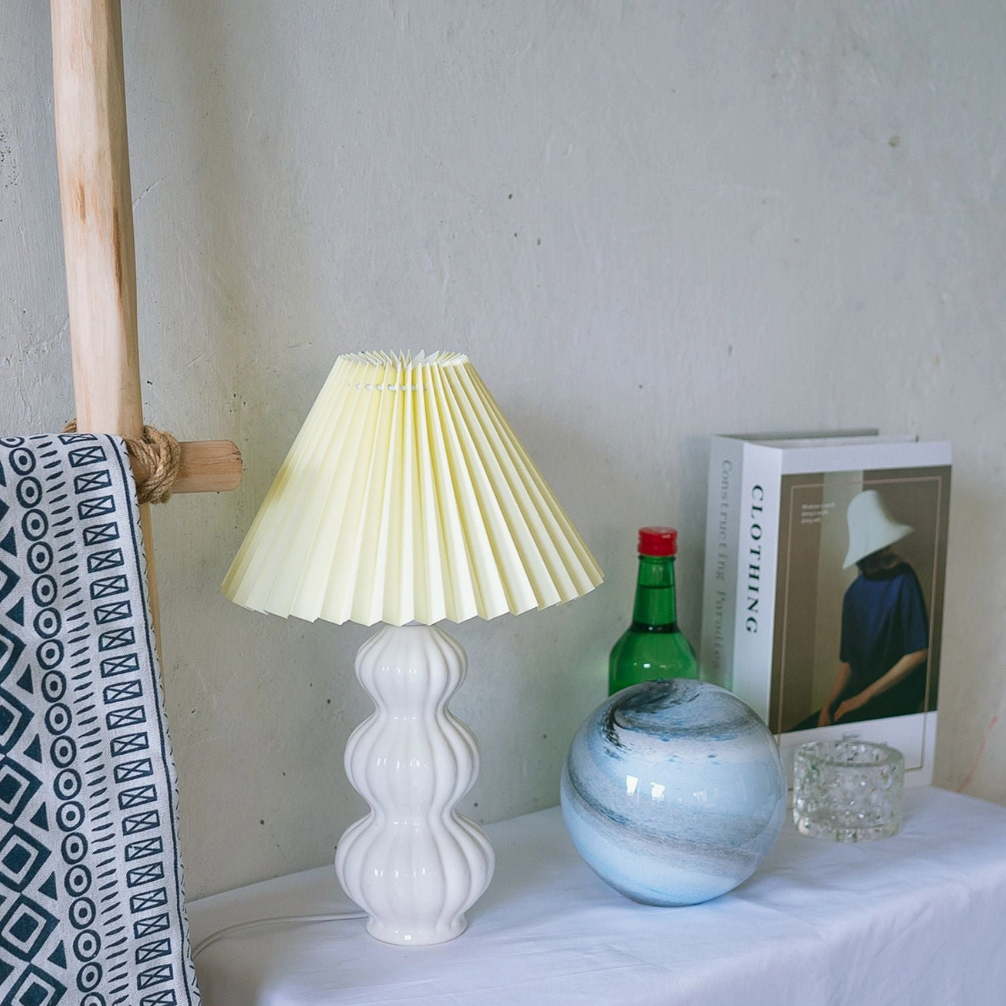 Luna pleated table lamp with cream yellow shade on bohemian home tabletop, white ceramic base styled with decorative props