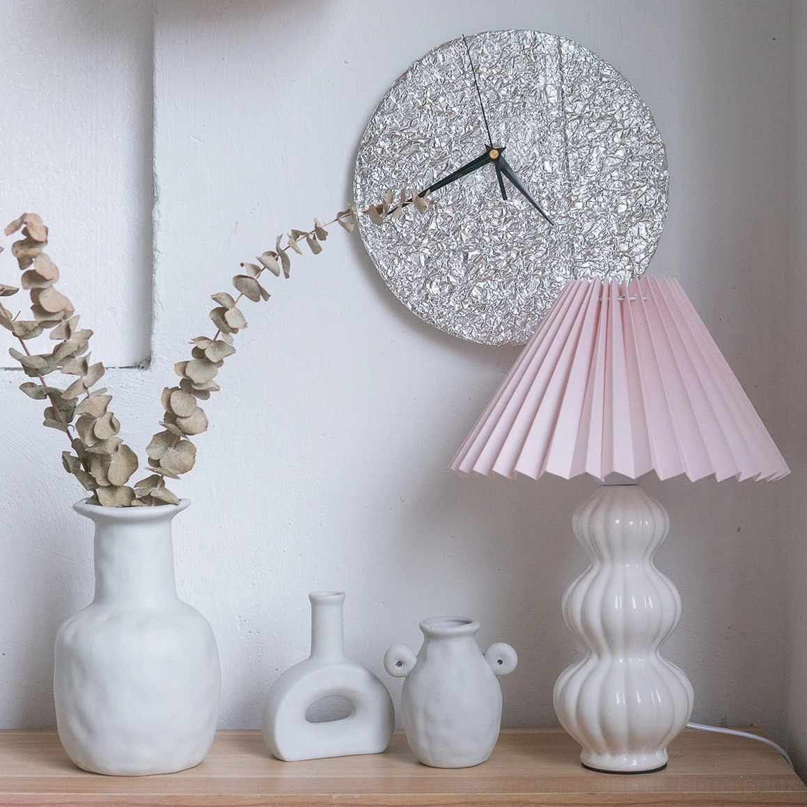 Luna pleated table lamp with dusty pink fabric shade, white curved ceramic base, minimalist wall shelf with dried florals