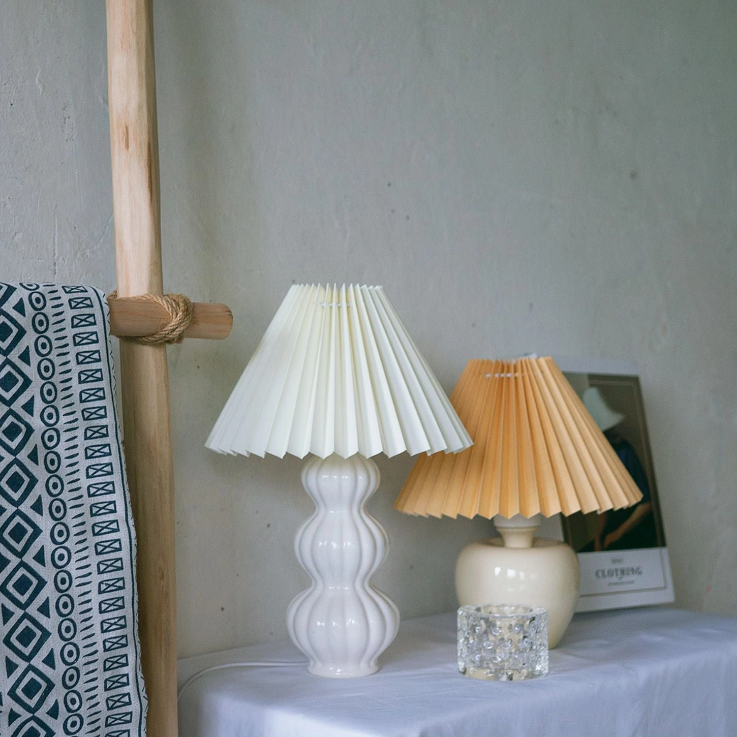 Two Luna pleated table lamps in different shade colors on bohemian home tabletop, white ceramic bases with fabric pleated shades