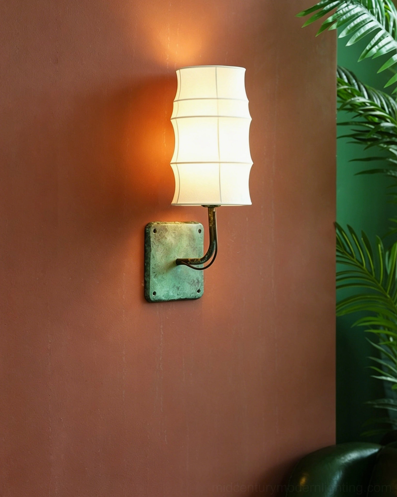 Side angle view of Maeve Lantern Wall Sconce with warm light on terracotta wall interior with green foliage