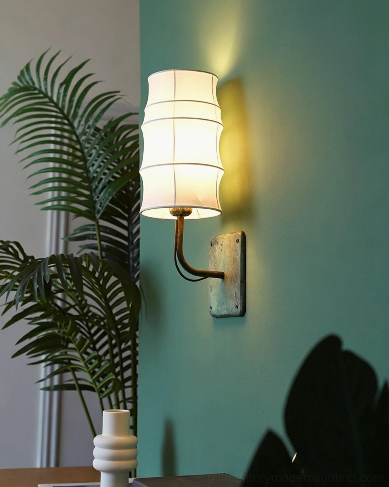 Verdigris wall-mounted lantern sconce with tiered fabric shade in teal green interior with plants