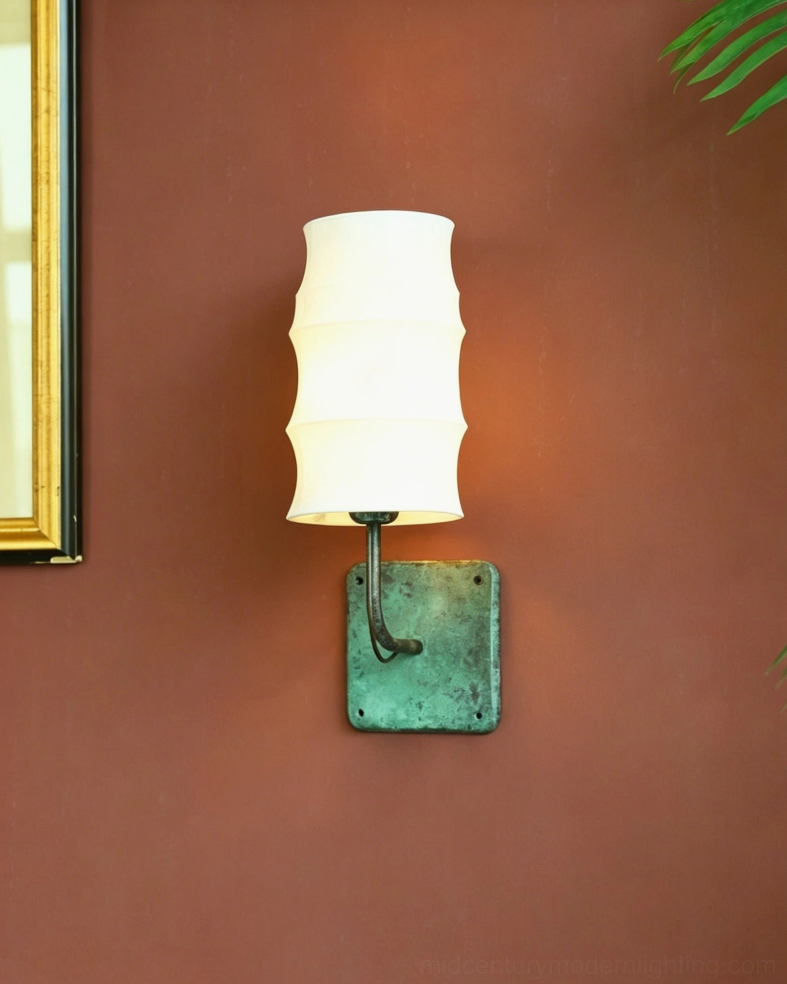 Architectural wall sconce with curved verdigris metal arm and off-white tiered shade on terracotta wall