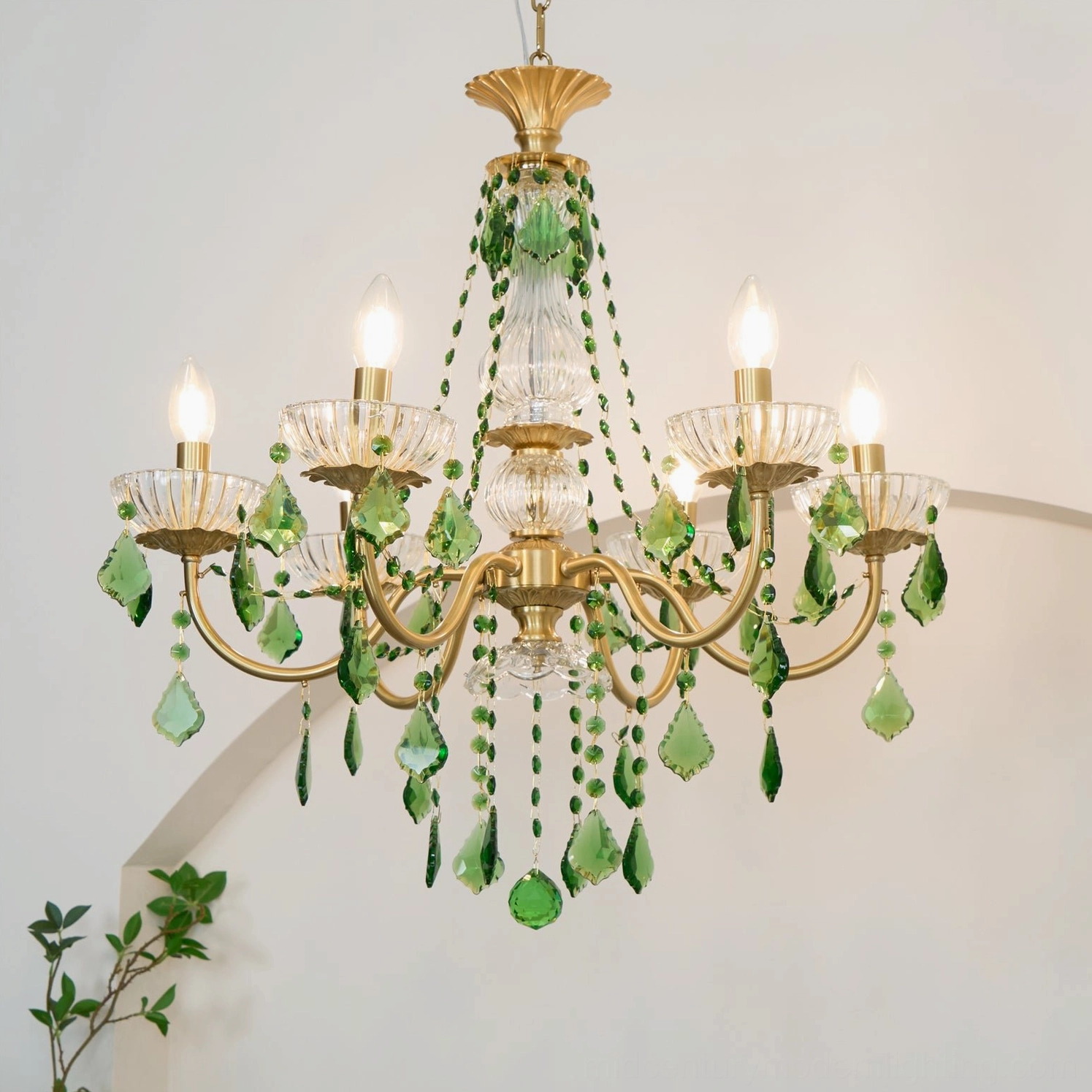 Magdalena brass chandelier with green crystals illuminated in home interior with warm lighting