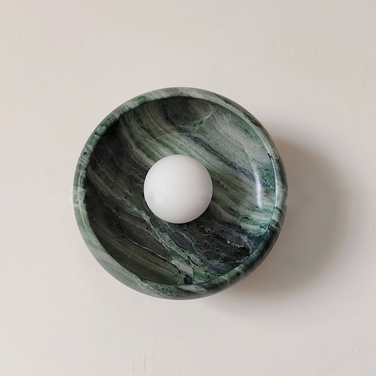 Contemporary marble wall lamp with natural stone base direct front view on neutral backdrop, round bowl-style holder